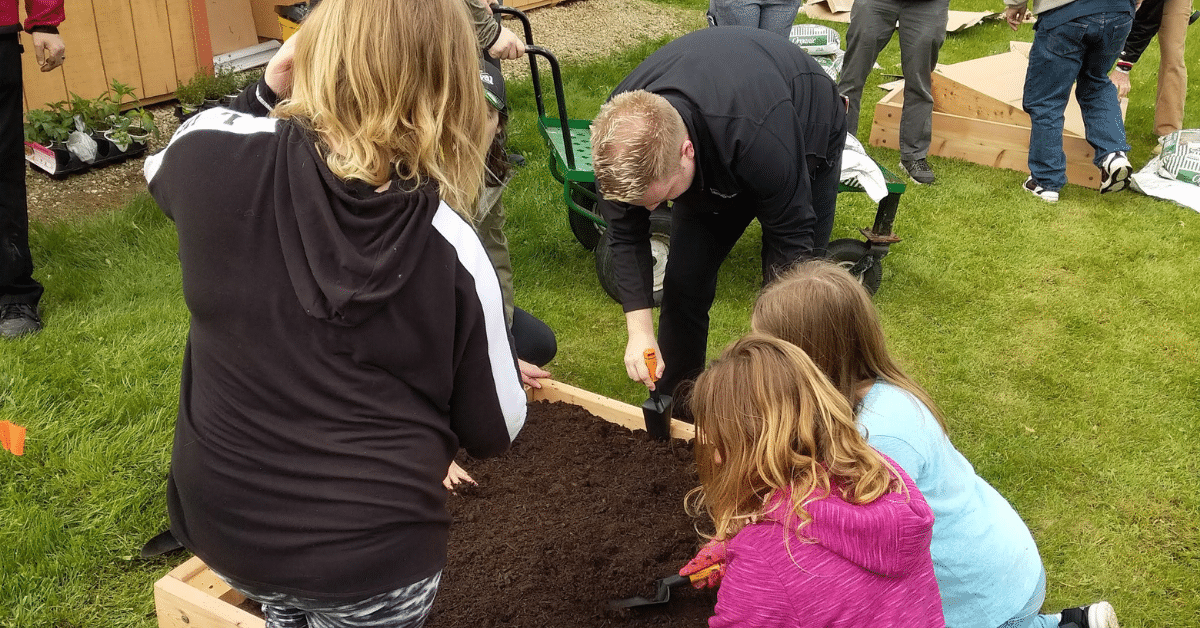 Three children and an adult dig in a garden bed