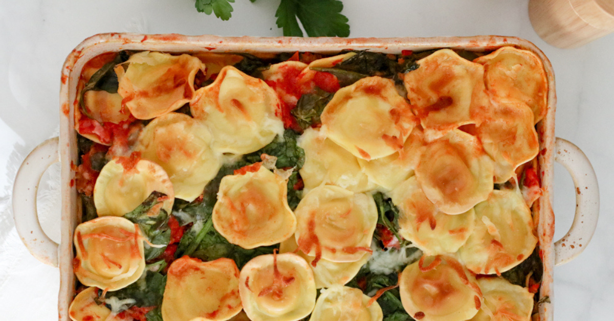 Ravioli Lasagna with melted cheese and spinach in white baking dish