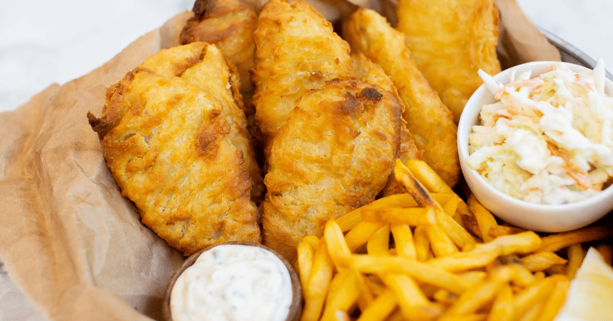 Fried fish fillets, french fries and coleslaw in a paper-lined basket with side of tartar sauce