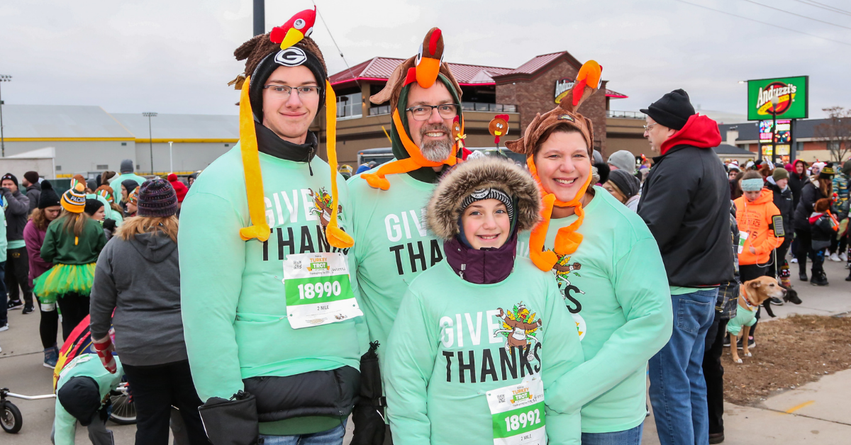 A family of four smiles, dressed in Festival Foods Turkey Trot shirts and turkey hats