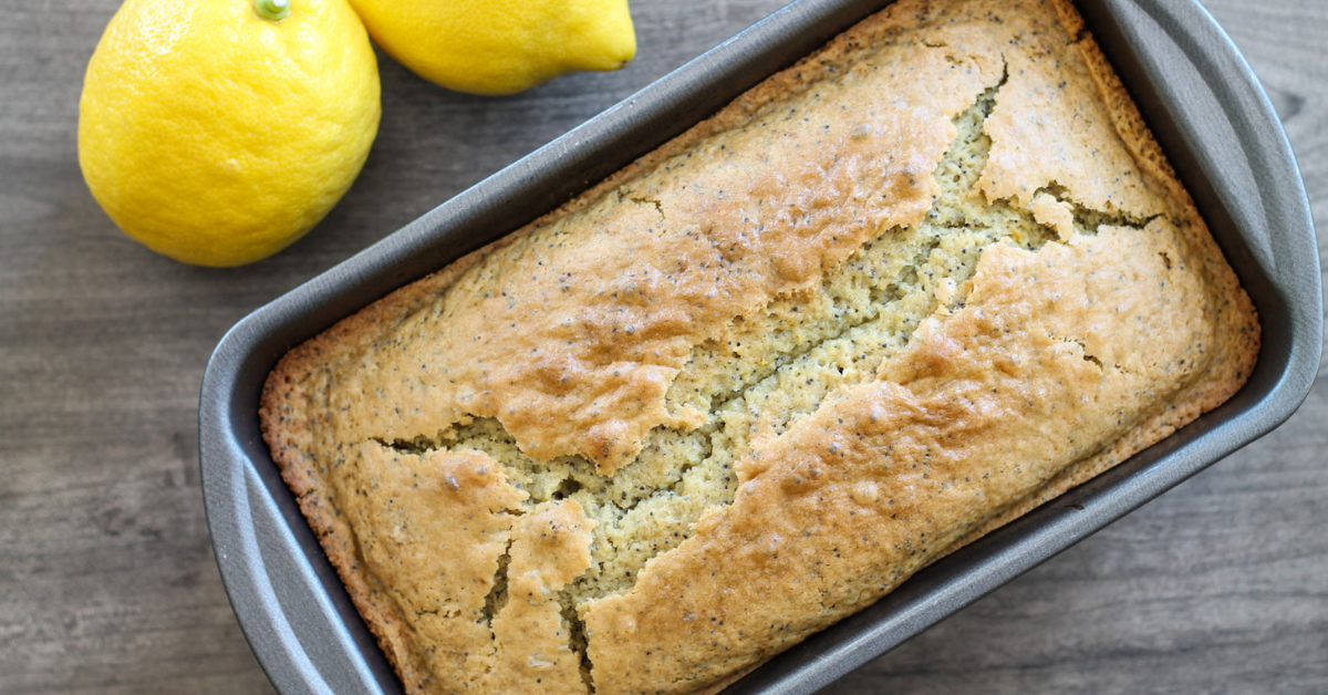Lemon poppy seed bread in loaf pan with whole lemons on the side